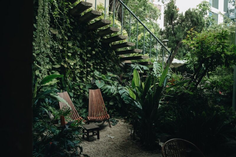 A couple of wooden chairs sitting next to a lush green wall