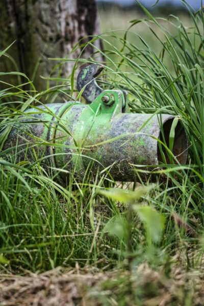 Green metallic object overgrown in tall grass.