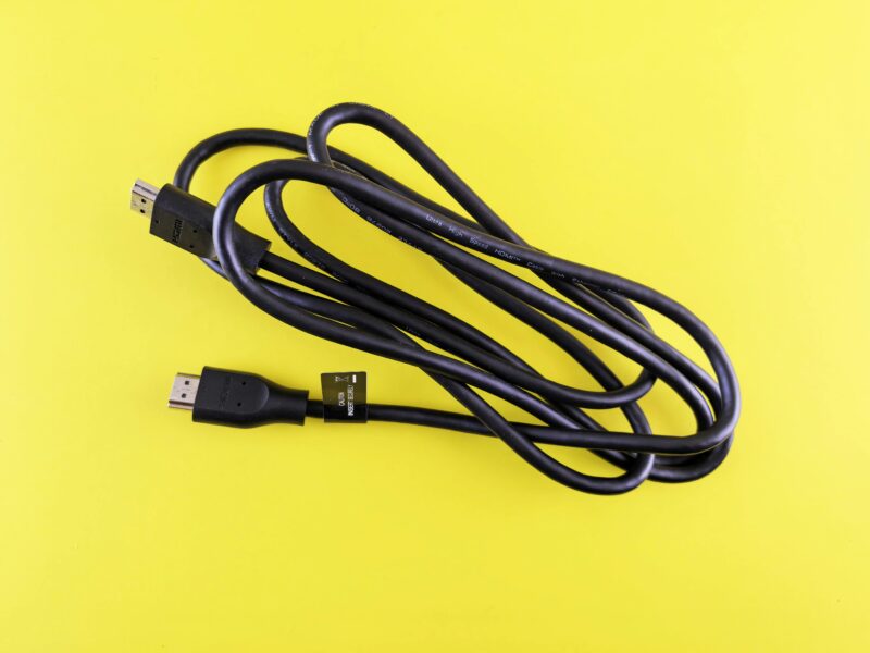 A neatly coiled black HDMI cable displayed on a vibrant yellow surface, ideal for tech visuals.