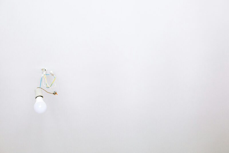 A minimalist light bulb with exposed wires hanging from a white ceiling.