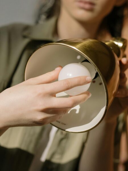 Detailed view of hands replacing a light bulb in a stylish golden lamp, emphasizing home decor and maintenance.