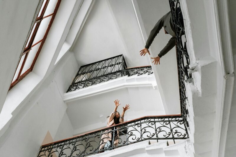 A romantic moment captured as a couple reaches towards each other across a wrought iron staircase banister indoors.