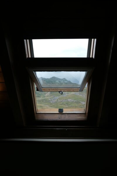 A breathtaking mountain landscape viewed through an open roof window indoors.