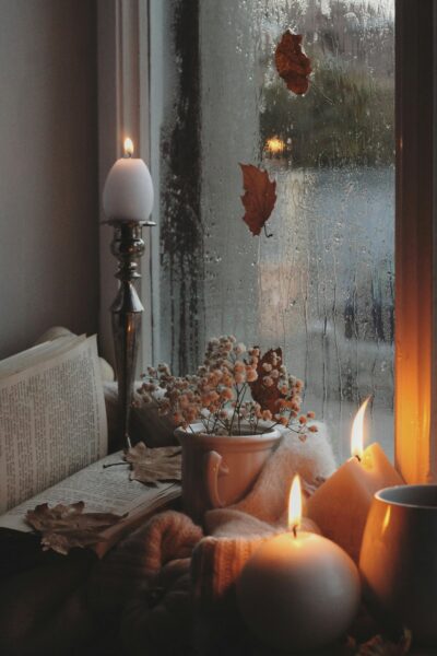 Warm and inviting autumn atmosphere by the window with candles, books, and raindrops.