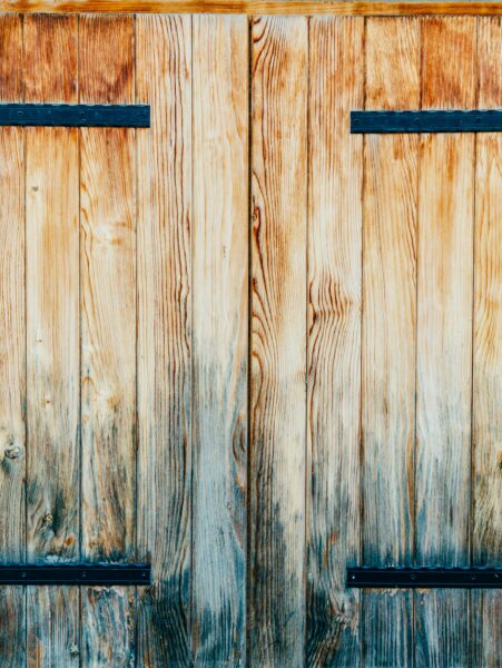 Close-up of rustic wooden barn doors featuring metal hinges with a weathered texture.