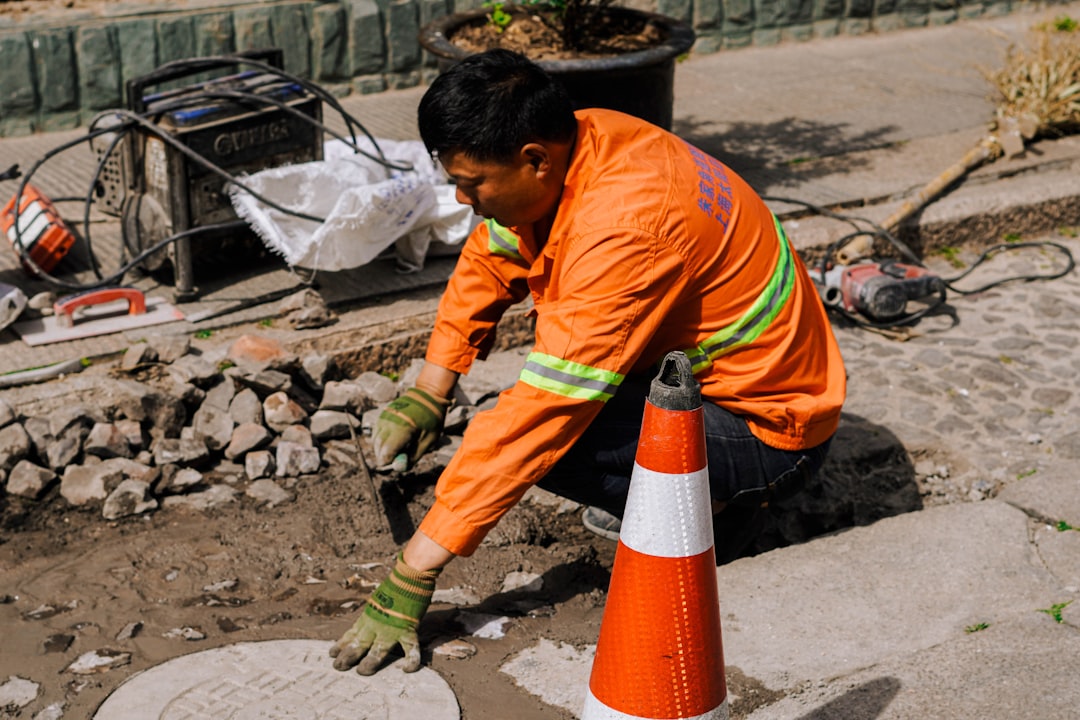 A worker in an orange shirt repairs a manhole cover.