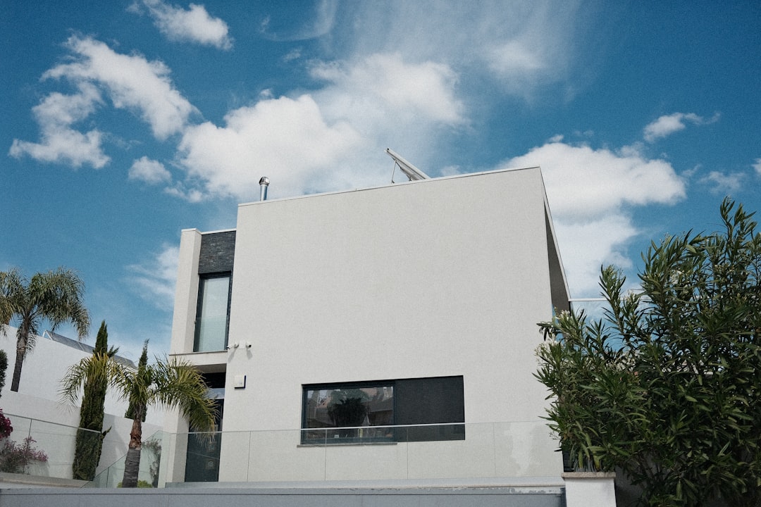 Modern white house with large windows and palm trees.