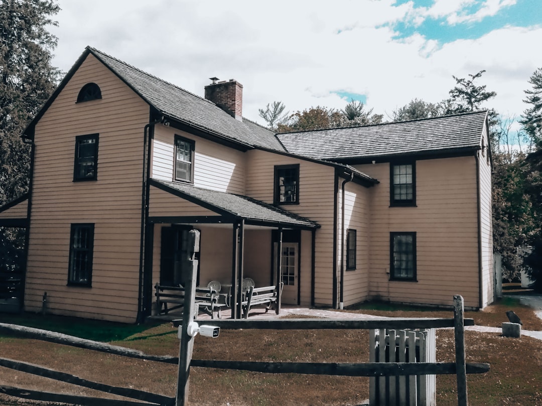 A historic light-colored house with a porch and wooden fence.