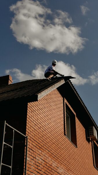 A contractor in protective gear repairing a roof on a sunny day.