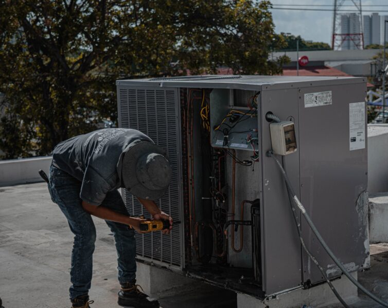 A technician is repairing an air conditioning unit on a rooftop, demonstrating skilled manual work.