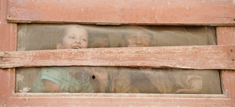 Afghan school boys peer through a window screen during a school visit by ANCOP members