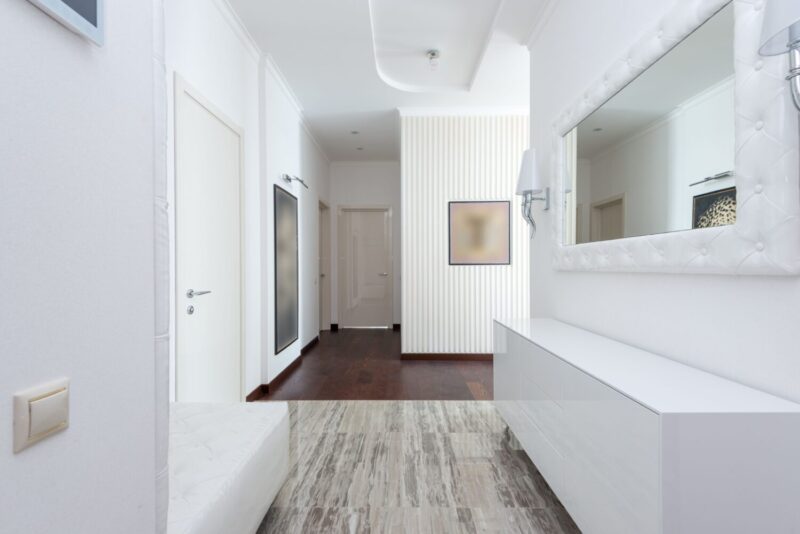 Bright corridor with contemporary design featuring white walls, minimal decor, and mirror.