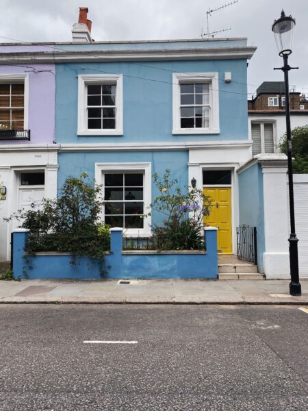Charming blue terraced house in London featuring a brightly colored yellow door and lush greenery.
