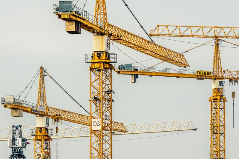 Cluster of yellow tower cranes at a construction site with a gloomy sky background.